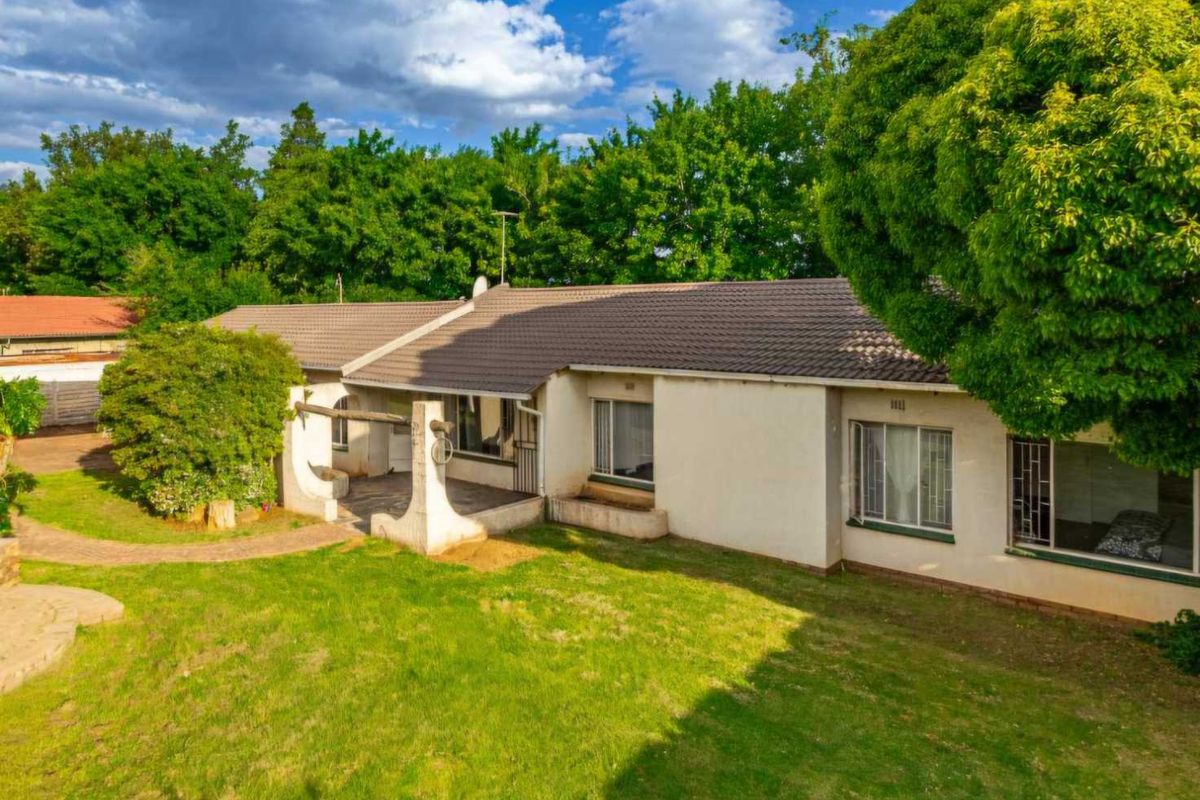 Rear view of the house featuring a tiled roof, covered patio area, and a spacious garden with established trees.