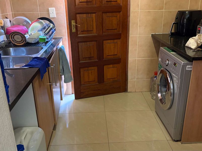 A functional laundry area featuring tiled walls and flooring, granite countertops, built-in cabinetry, and a double basin sink.