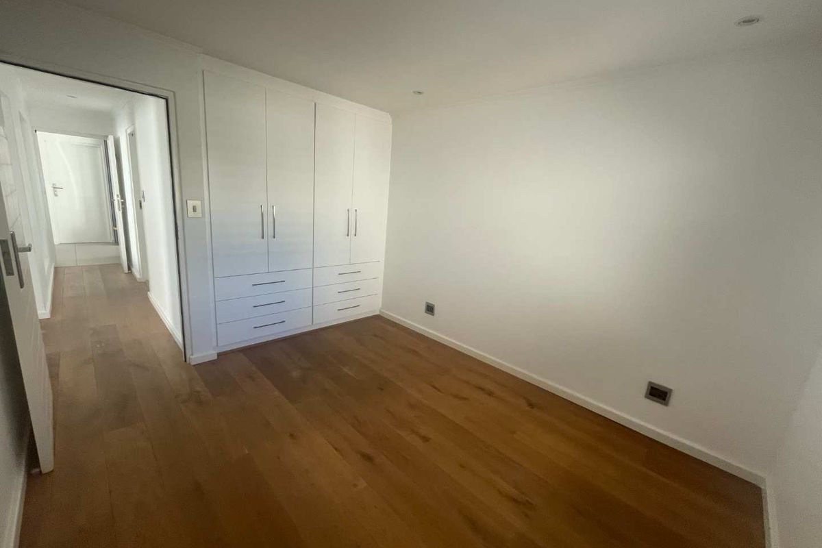 A bright, empty bedroom featuring polished hardwood flooring, built-in white cabinetry, and recessed ceiling lighting, offering a clean and neutral space.
