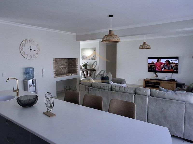 Spacious open-plan living area featuring a modern kitchen with island, subway tile backsplash, and a built-in brick fireplace, seamlessly flowing into the lounge.