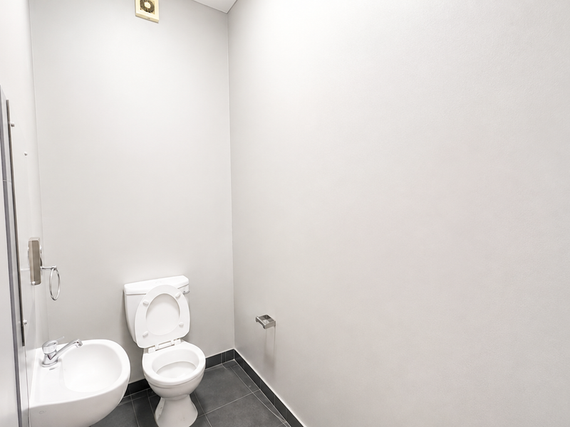 A clean, minimalist bathroom featuring a white toilet, wall-mounted basin, and neutral tiled flooring with an integrated extractor fan.