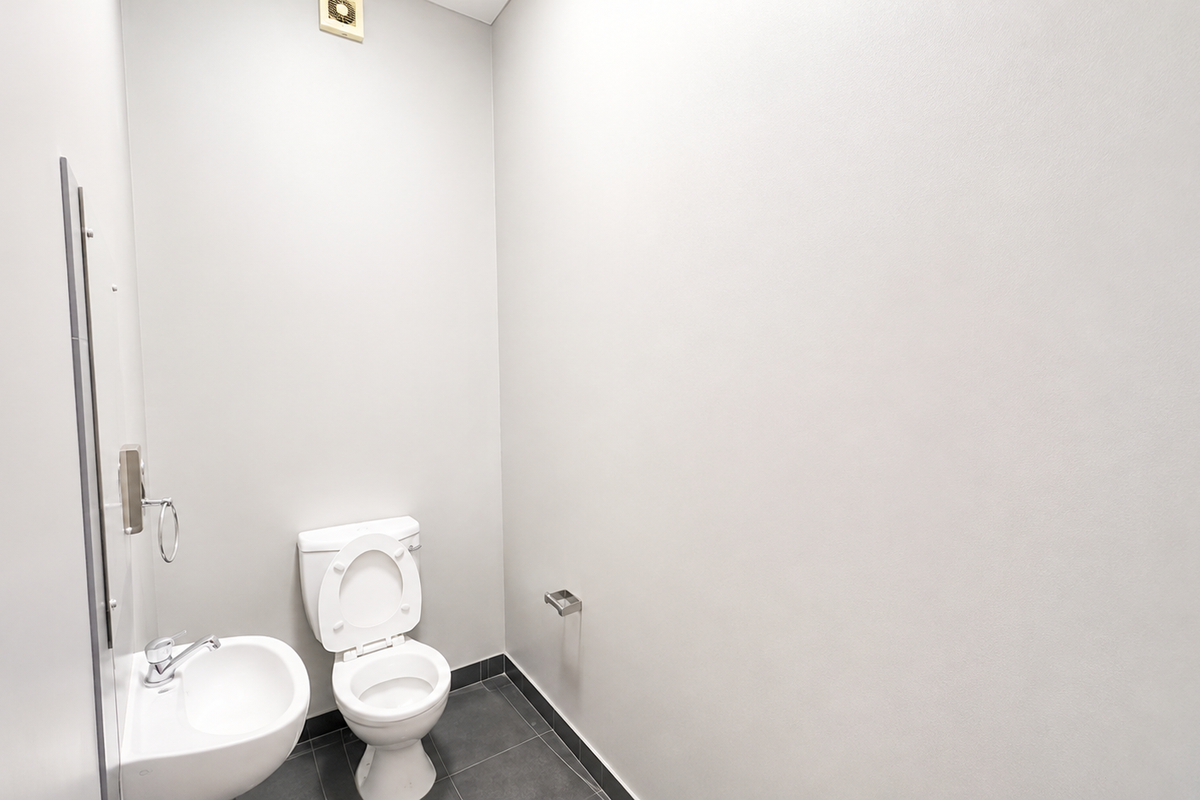 A clean, minimalist bathroom featuring a white toilet, wall-mounted basin, and neutral tiled flooring with an integrated extractor fan.