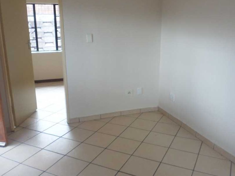 An empty living area featuring neutral wall paint and ceramic floor tiles, with a doorway leading to an adjacent room.
