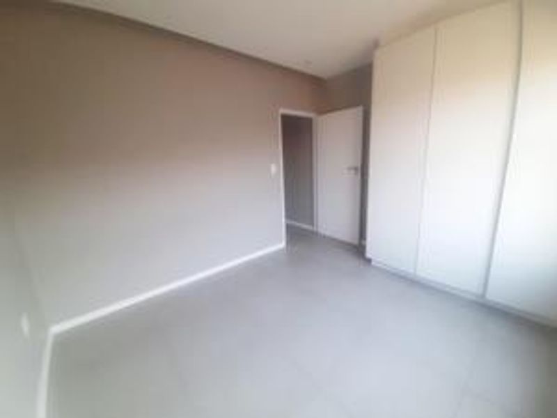 A clean, empty bedroom featuring neutral wall tones, tiled flooring, and a large built-in wardrobe with white cabinetry.