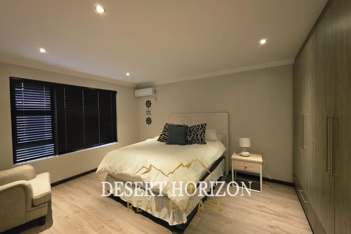 A well-maintained bedroom featuring modern laminate flooring, extensive built-in cabinetry, recessed lighting, and a wall-mounted split-system air conditioning unit.