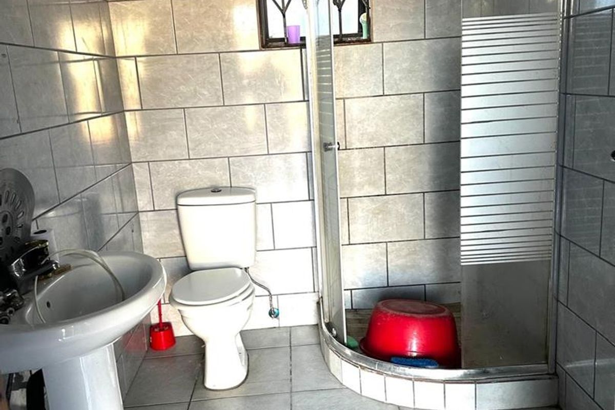 A functional bathroom featuring a pedestal basin, a standard toilet, and a corner shower enclosure with tiled walls and flooring.
