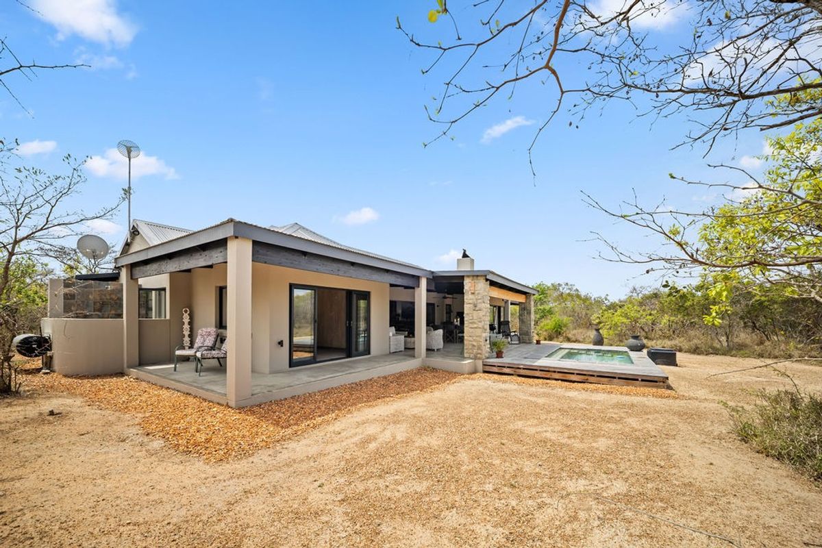 Rear view of the property featuring a covered patio, timber decking, and a swimming pool set against a natural landscape.