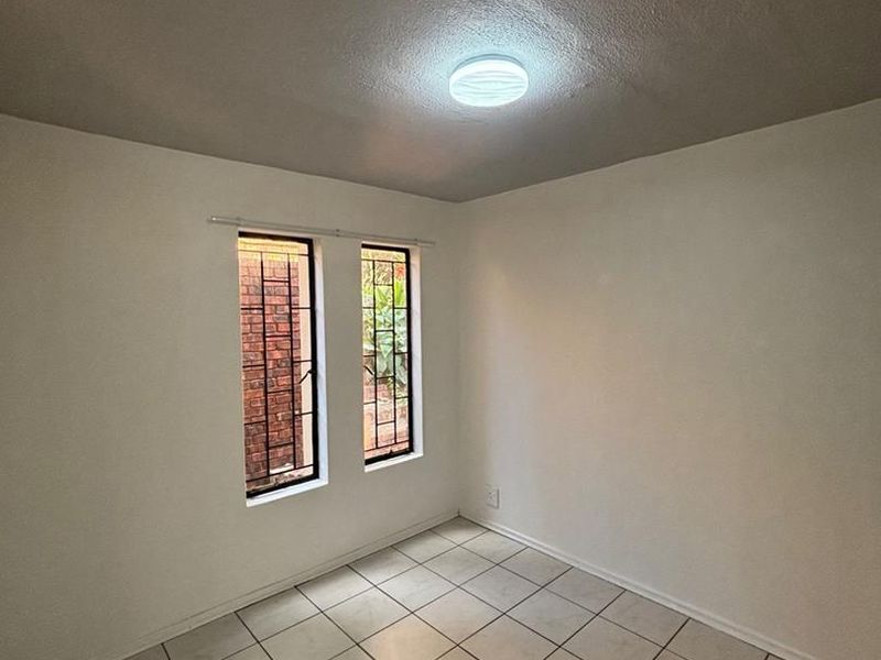 A clean, empty bedroom featuring neutral tiled flooring and windows fitted with security bars, offering a blank canvas for personalization.