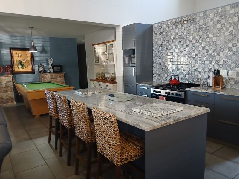 Spacious open-plan kitchen featuring a large island with granite countertops, modern cabinetry, and a decorative tiled backsplash, seamlessly flowing into the living area.