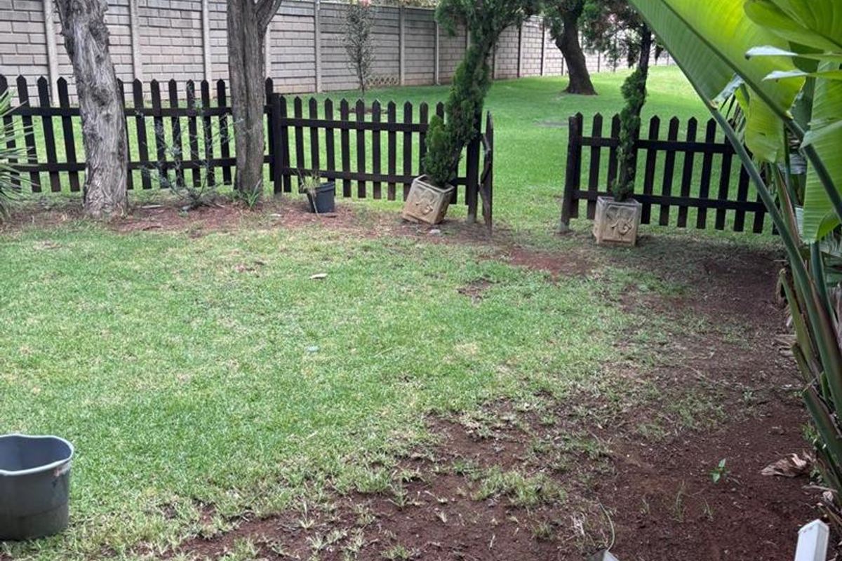 A private rear garden featuring a tiled patio area, established trees, and a perimeter fence, offering a quiet outdoor space for the townhouse.
