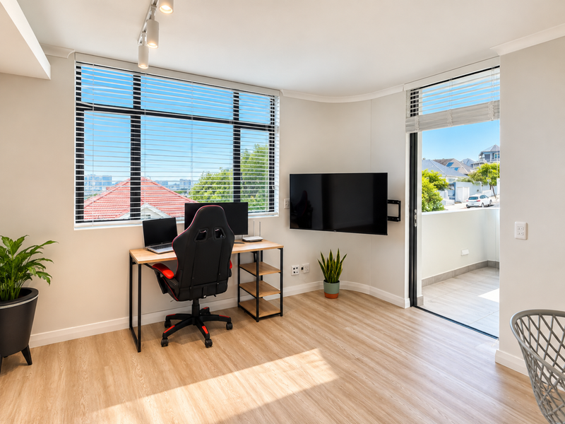 A bright, modern home office featuring laminate flooring, track lighting, and a sliding glass door leading to a private balcony.