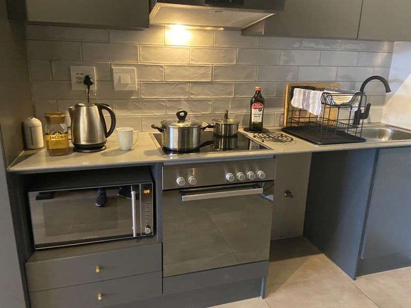 Modern kitchen featuring grey cabinetry, subway tile backsplash, built-in oven, electric hob, extractor fan, and a sleek stainless steel sink with a matte black faucet.