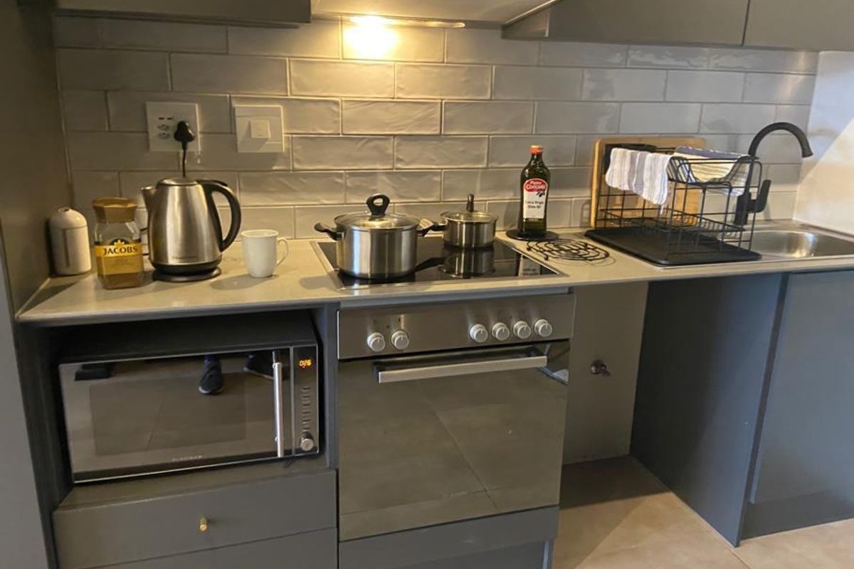 Modern kitchen featuring grey cabinetry, subway tile backsplash, built-in oven, electric hob, extractor fan, and a sleek stainless steel sink with a matte black faucet.