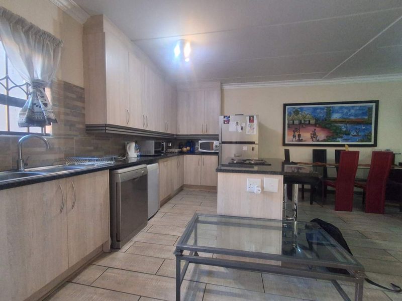Open-plan kitchen and dining area featuring light wood cabinetry, granite countertops, tiled flooring, and a functional kitchen island.