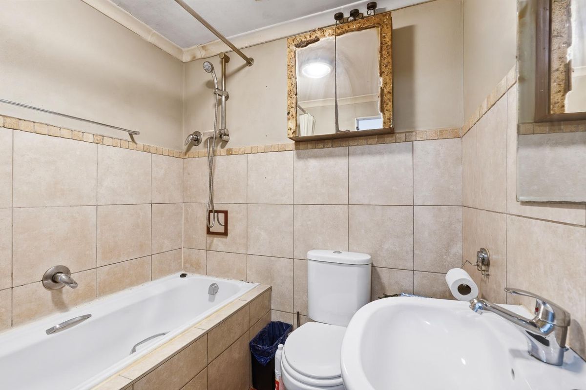 A functional bathroom featuring a bathtub with shower attachment, a standard toilet, a washbasin, and tiled wall finishes.
