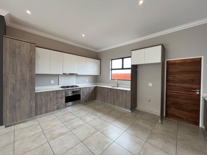 Modern kitchen featuring two-tone cabinetry, gas hob, under-counter oven, extractor fan, and tiled flooring in a clean, open-plan layout.