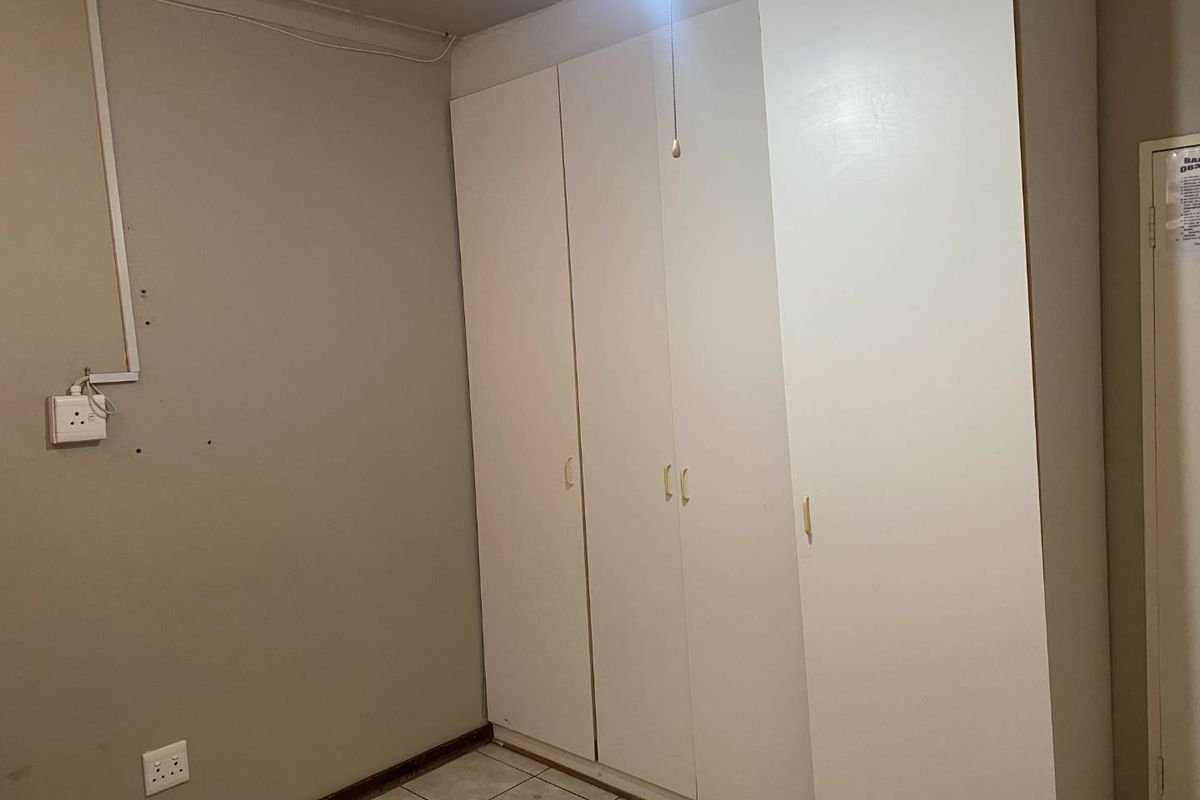 A bedroom featuring built-in cupboards and tiled flooring, requiring minor cosmetic repairs to wall surfaces and electrical finishes.