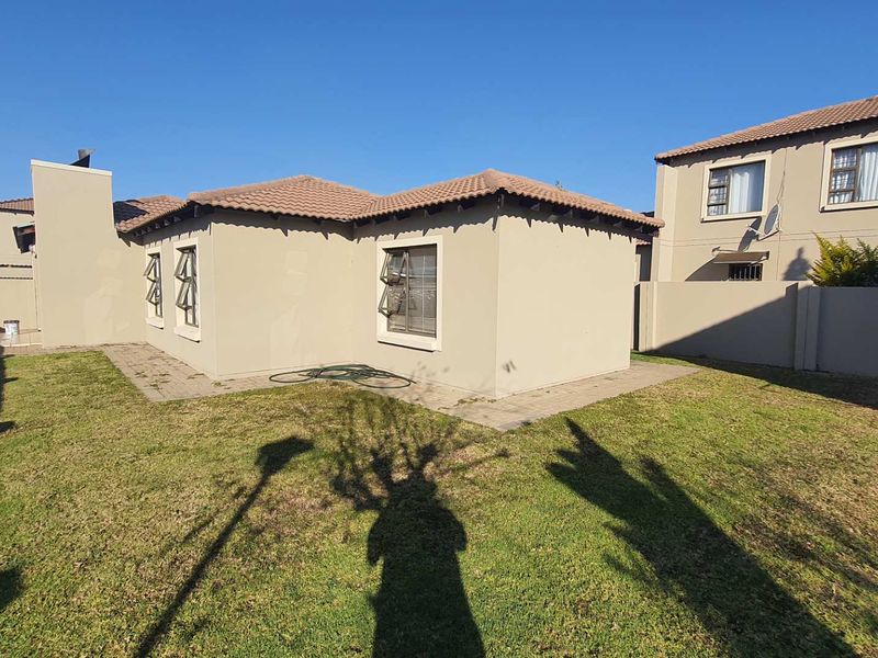 Rear view of the townhouse featuring a private garden, paved walkway, and tiled roof structure.