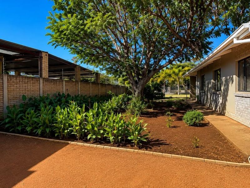 A well-maintained rear garden area featuring a brick boundary wall, mature tree, paved walkway, and an integrated water tank system.