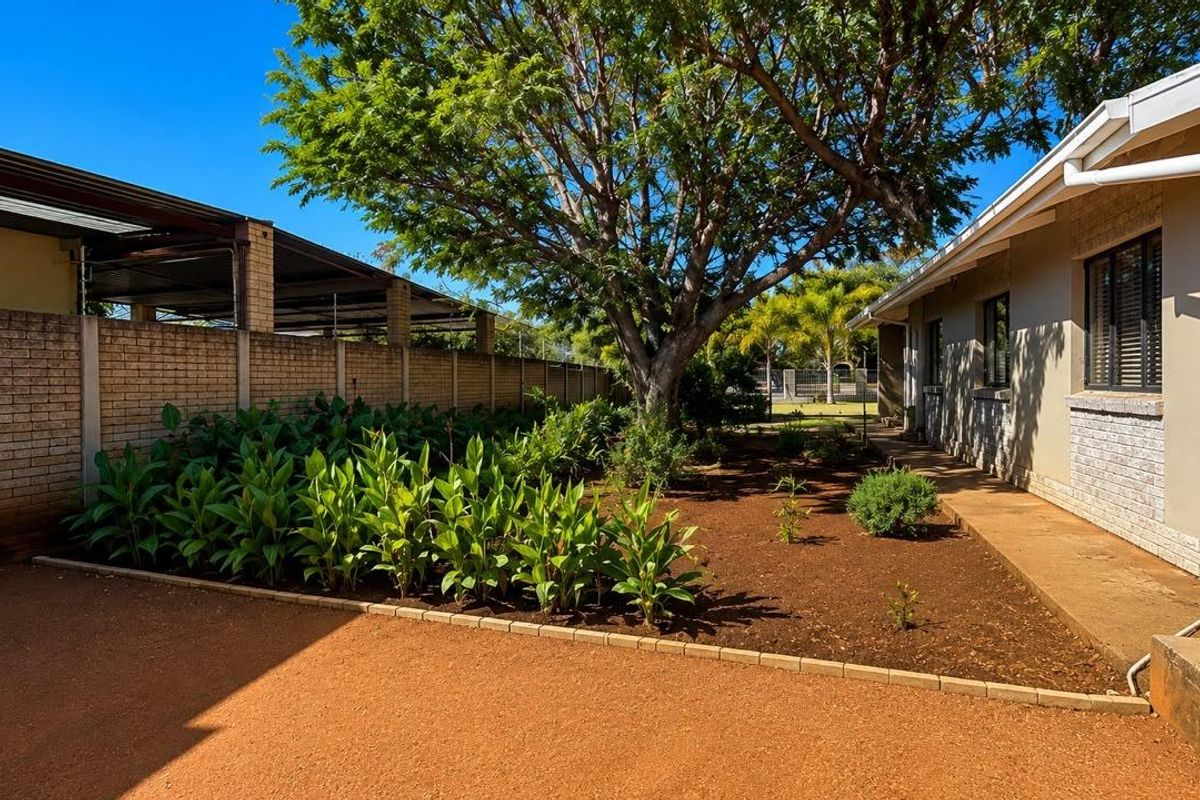 A well-maintained rear garden area featuring a brick boundary wall, mature tree, paved walkway, and an integrated water tank system.