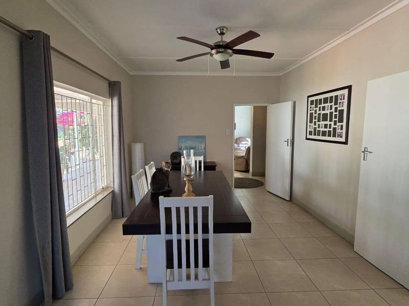 A functional dining room featuring tiled flooring, a ceiling fan, and large windows with security bars, providing a bright and practical space.