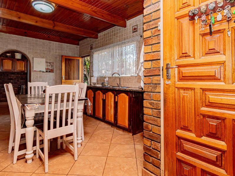 Open-plan living and kitchen area featuring exposed timber ceilings, tiled floors, brick accents, and traditional wooden cabinetry with granite countertops.
