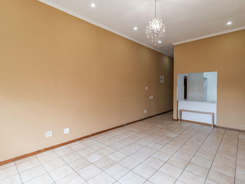 An empty living area featuring tiled flooring, recessed downlights, a decorative chandelier, and a convenient pass-through window connecting to the kitchen area.