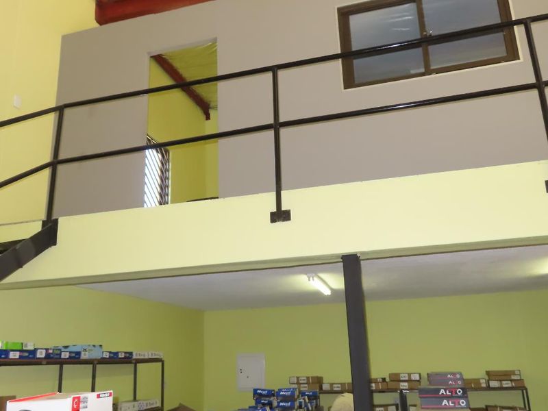 Industrial utility space featuring a mezzanine level with metal railing, exposed steel roof structure, and functional fluorescent lighting.