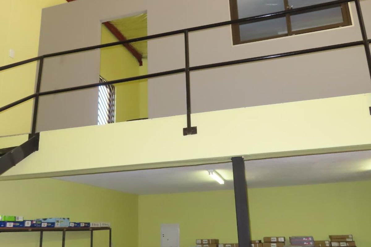 Industrial utility space featuring a mezzanine level with metal railing, exposed steel roof structure, and functional fluorescent lighting.