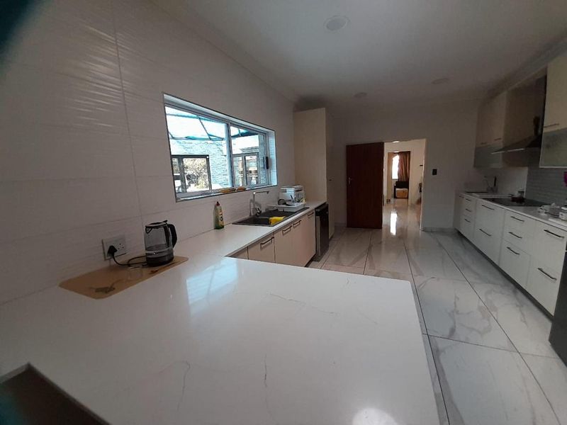 Modern kitchen featuring sleek white cabinetry, quartz countertops, large format marble-look floor tiles, and integrated appliances with ample workspace.