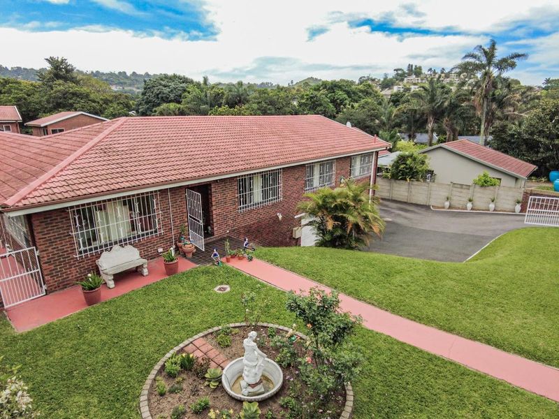 Aerial view of a brick house featuring a tiled roof, security bars on windows, a paved driveway, and a well-maintained garden with a central fountain.