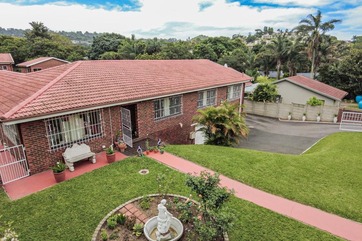 Aerial view of a brick house featuring a tiled roof, security bars on windows, a paved driveway, and a well-maintained garden with a central fountain.