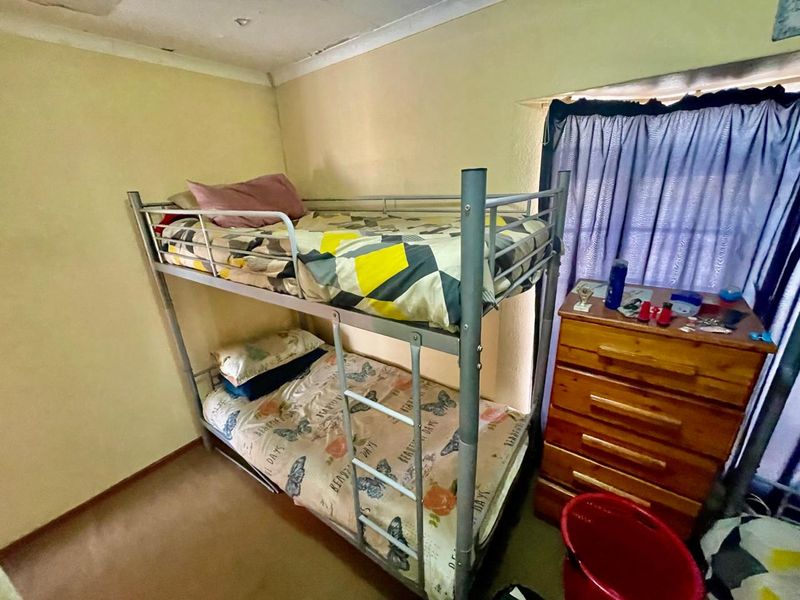 A compact bedroom featuring a coved ceiling and window, currently showing signs of ceiling water damage and paint deterioration requiring maintenance.