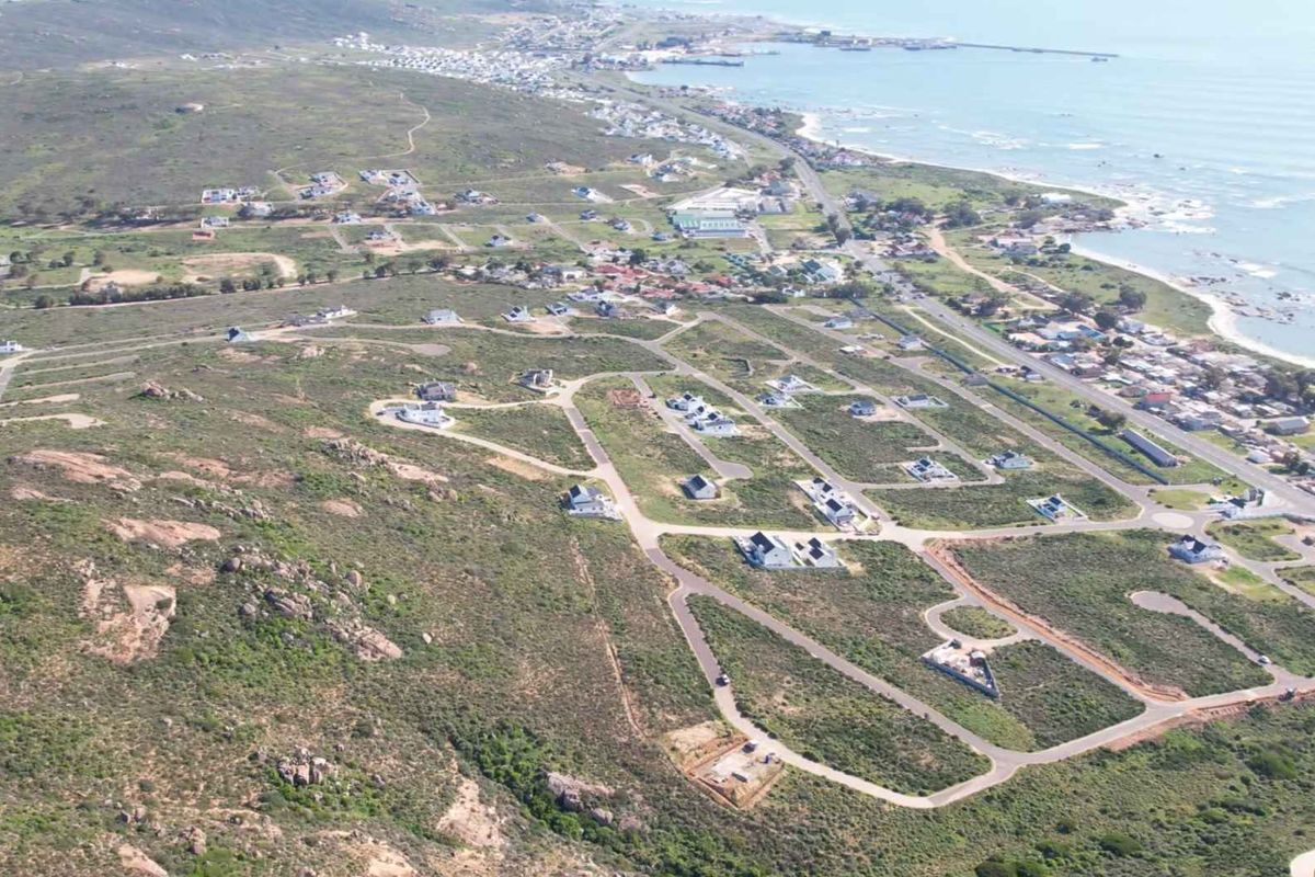 An aerial view of a coastal residential development featuring established road infrastructure and scattered vacant plots near the coastline.