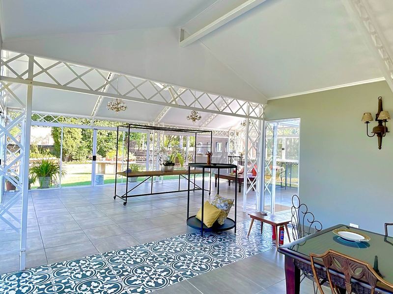 Spacious enclosed patio featuring a vaulted ceiling, decorative metal lattice framework, and a combination of neutral and patterned floor tiles with garden access.
