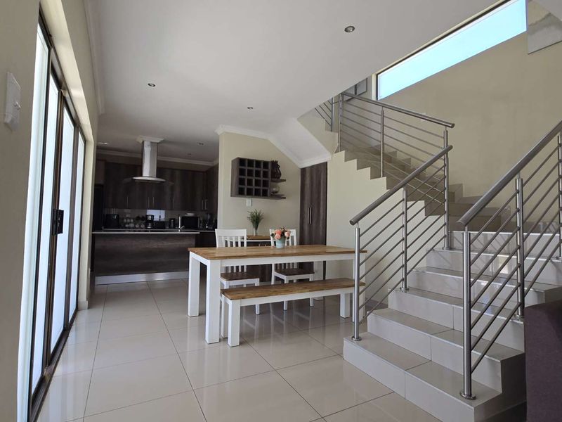 Modern open-plan living area featuring tiled floors, a sleek staircase with stainless steel railings, and a contemporary kitchen with built-in cabinetry.