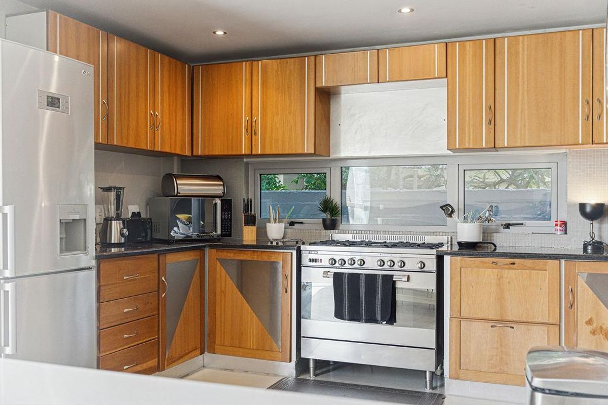 A functional kitchen featuring wooden cabinetry, granite countertops, and a stainless steel gas range with an integrated extractor fan.