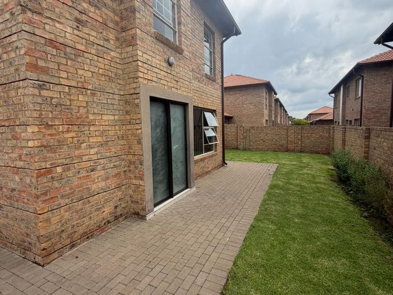 Rear view of the apartment featuring a face brick facade, a paved patio area, and a private lawn enclosed by a perimeter brick wall.