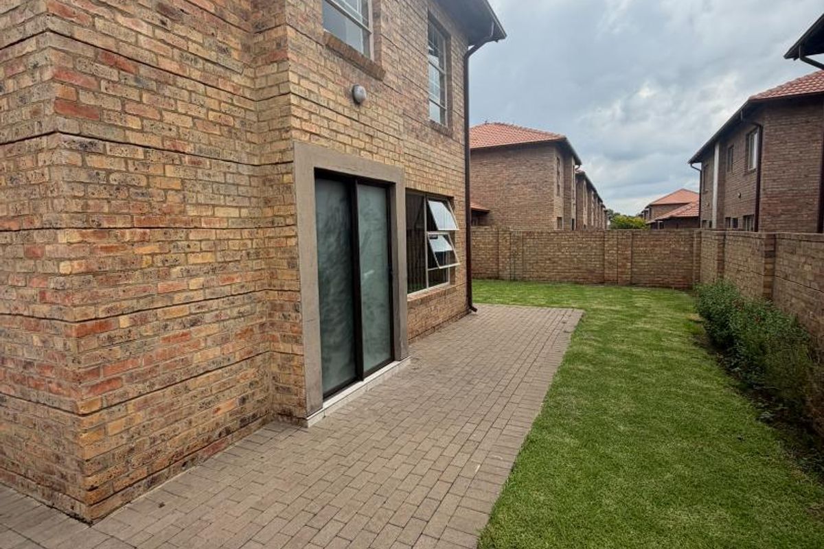Rear view of the apartment featuring a face brick facade, a paved patio area, and a private lawn enclosed by a perimeter brick wall.