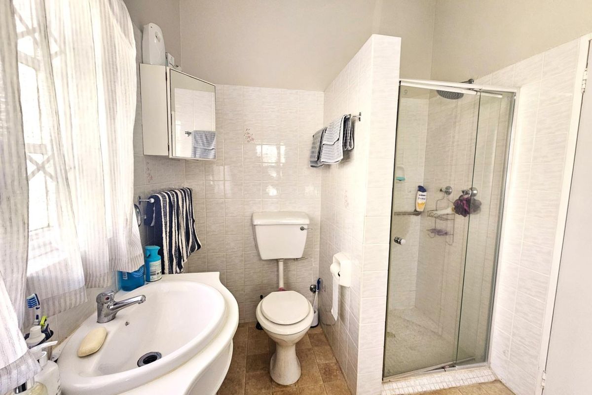 A functional bathroom featuring a glass-enclosed shower, pedestal basin, and toilet with neutral wall tiling.