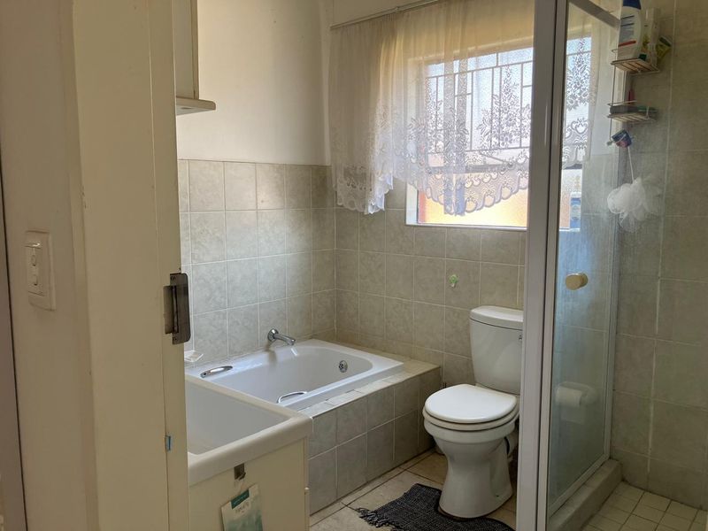 A functional bathroom featuring a built-in bathtub, separate shower enclosure, and toilet, finished with neutral wall and floor tiling.