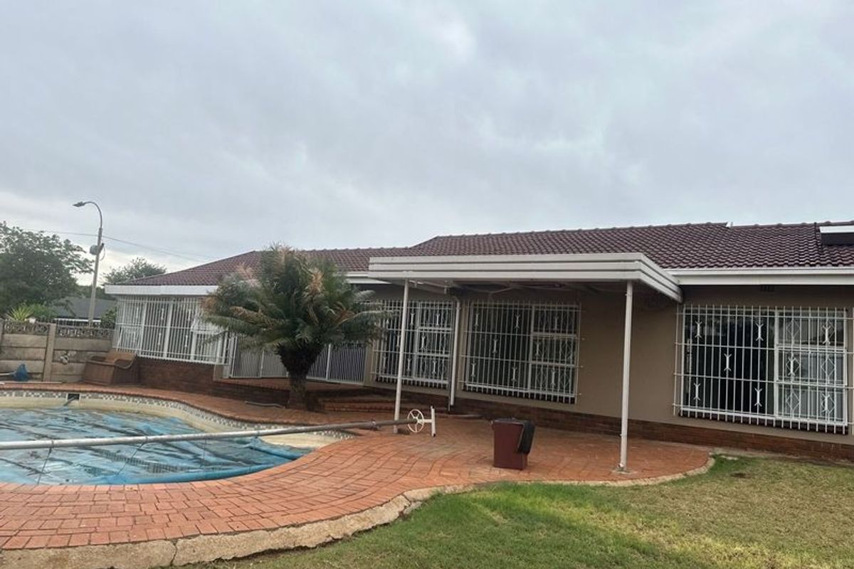 Rear exterior view featuring a swimming pool, brick paved patio area, and a covered veranda with security bars on the windows.
