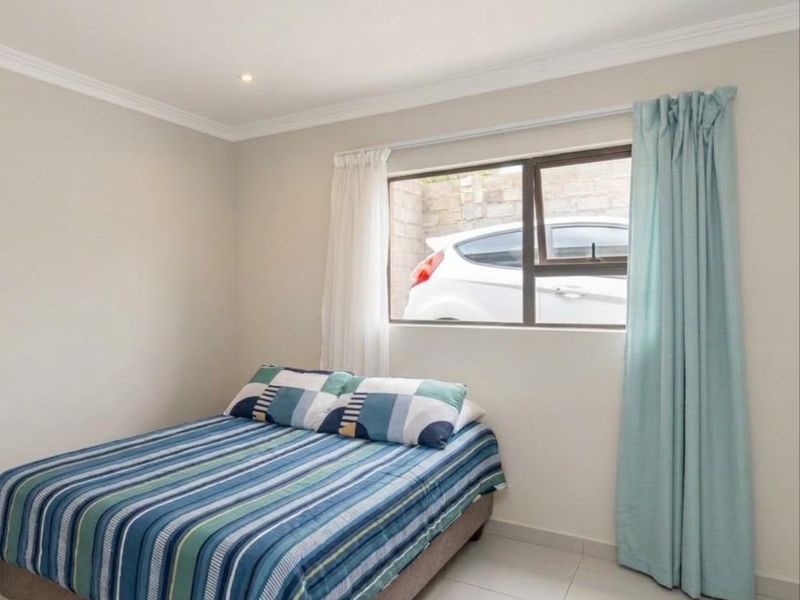 A well-maintained bedroom featuring neutral wall tones, tiled flooring, recessed downlighting, and an aluminium-framed window.