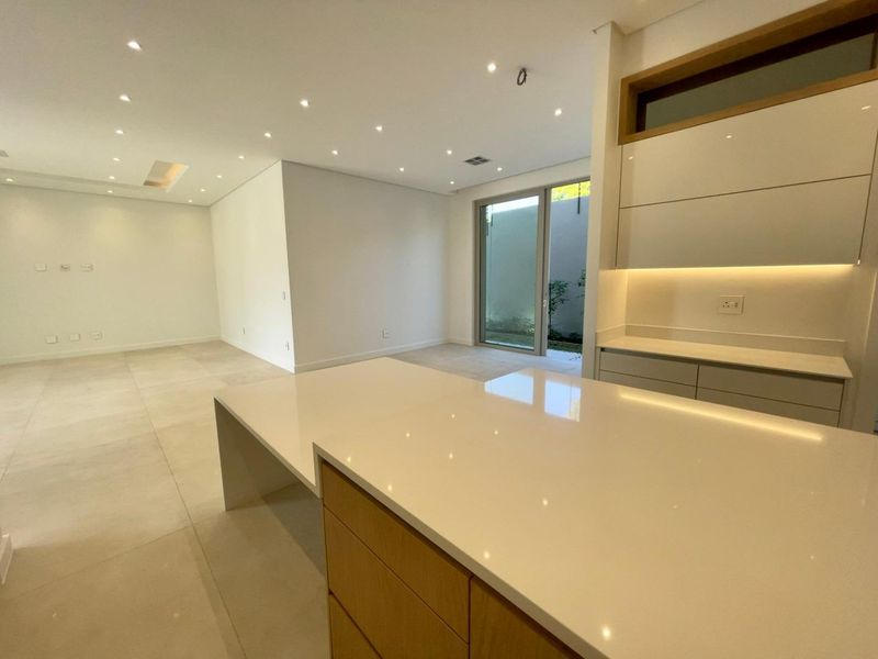 Modern open-plan kitchen and living area featuring sleek cabinetry, stone countertops, recessed lighting, and large sliding glass doors leading to an outdoor space.
