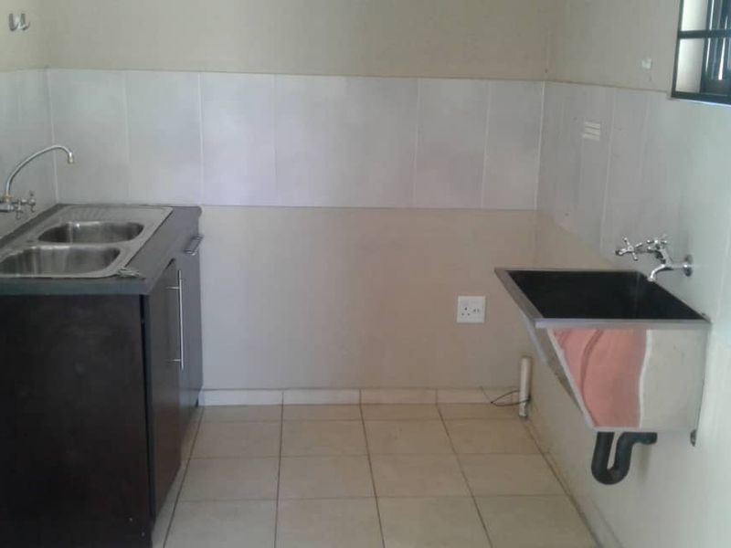A functional laundry area featuring a double stainless steel sink, a wall-mounted utility basin, tiled splashbacks, and tiled flooring.