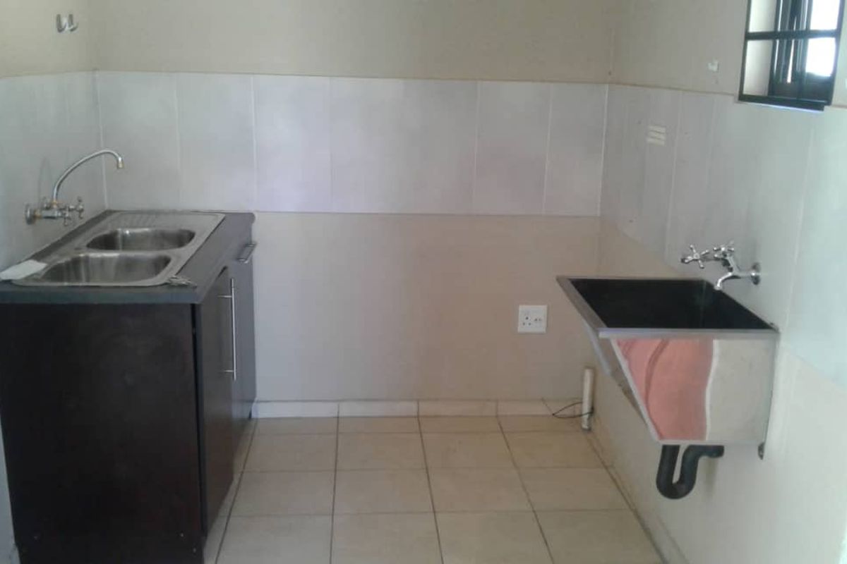 A functional laundry area featuring a double stainless steel sink, a wall-mounted utility basin, tiled splashbacks, and tiled flooring.