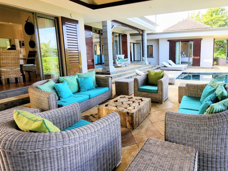 Spacious covered patio featuring stone tile flooring and stone columns, providing seamless indoor-outdoor flow to the adjacent swimming pool area.
