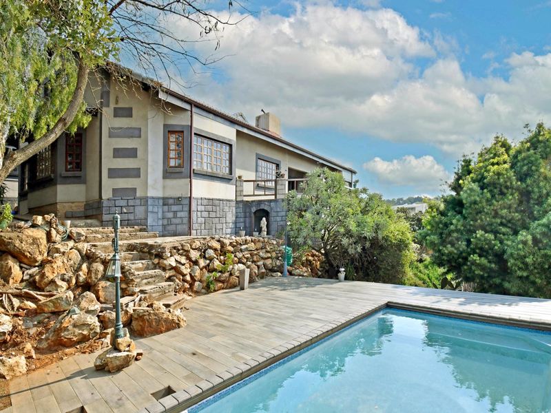 Rear exterior view featuring a swimming pool, timber decking, and a rustic stone retaining wall leading to the main house structure.