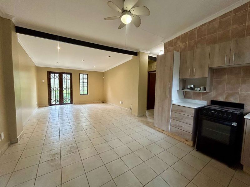 Spacious open-plan living area featuring tiled flooring, a ceiling fan, and a functional kitchen with built-in cabinetry and a stove.