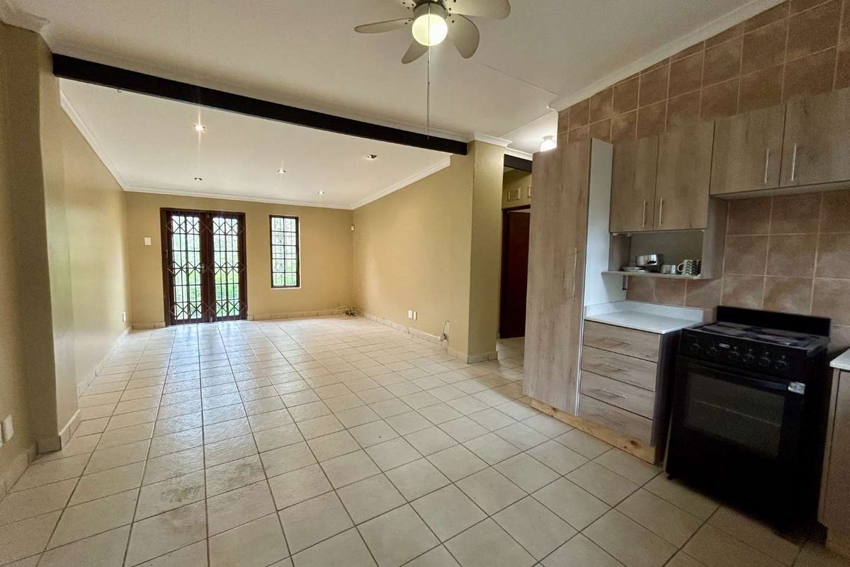 Spacious open-plan living area featuring tiled flooring, a ceiling fan, and a functional kitchen with built-in cabinetry and a stove.